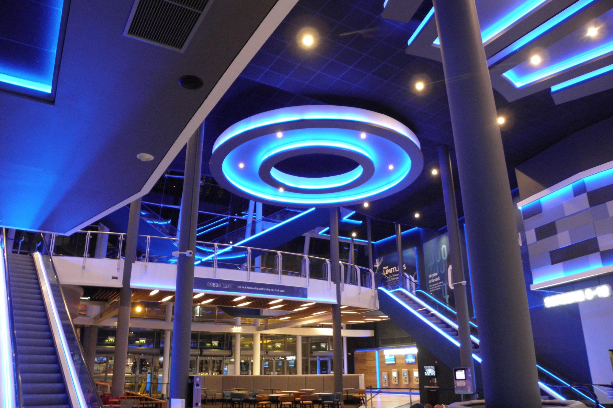 Blue LED lighting inside cinema foyer with circular Blue LED feature with downlights and blue LED escalator lighting.