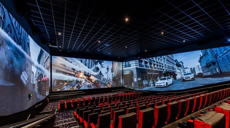 A modern cinema auditorium with panoramic screens and red seating rows.